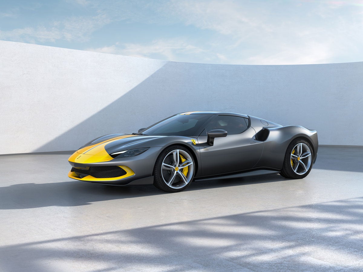 A grey Ferrari with a yellow stripe on the hood, parked outdoors against a curved white wall under a blue sky.