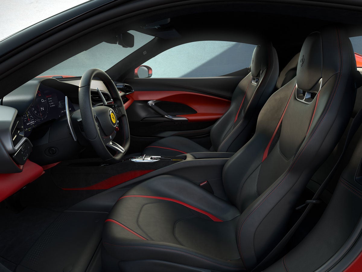 Red and black luxury car interior with two seats, a steering wheel with a yellow badge, and a digital dashboard.