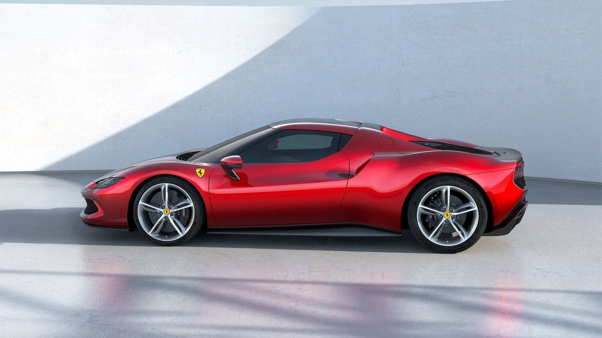 A sleek red Ferrari sports car, viewed from the side, parked against a white wall with sunlight casting shadows.