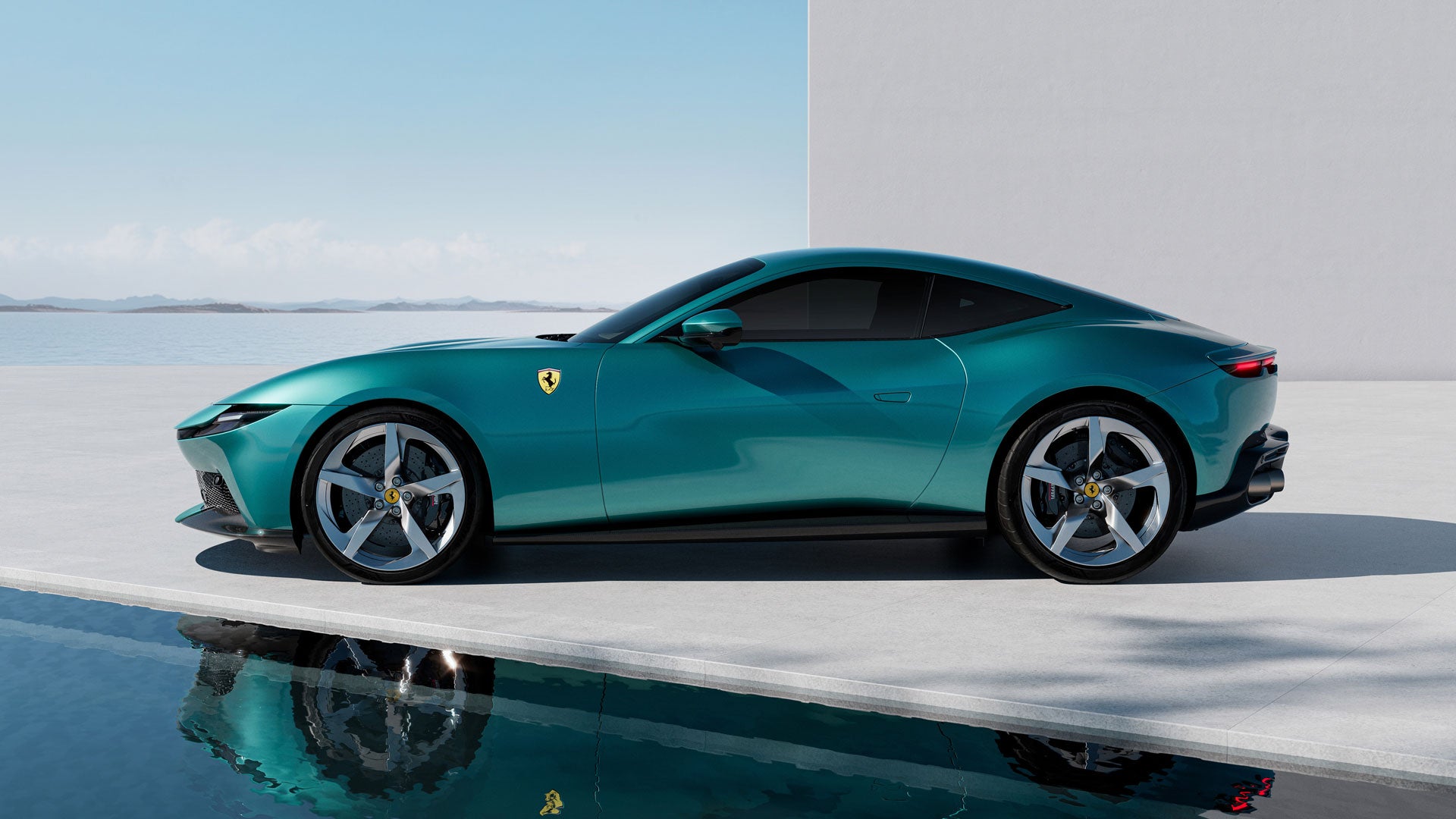 Side view of a sleek teal Ferrari parked on a concrete edge above reflective water, with the sea in the background.