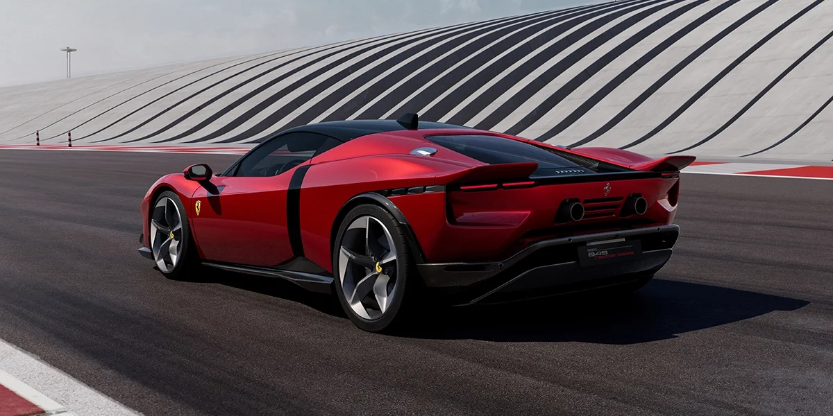 Rear three-quarter view of the Ferrari 849 Testarossa in red driving on a racetrack, showing taillights, diffuser, and exhausts.